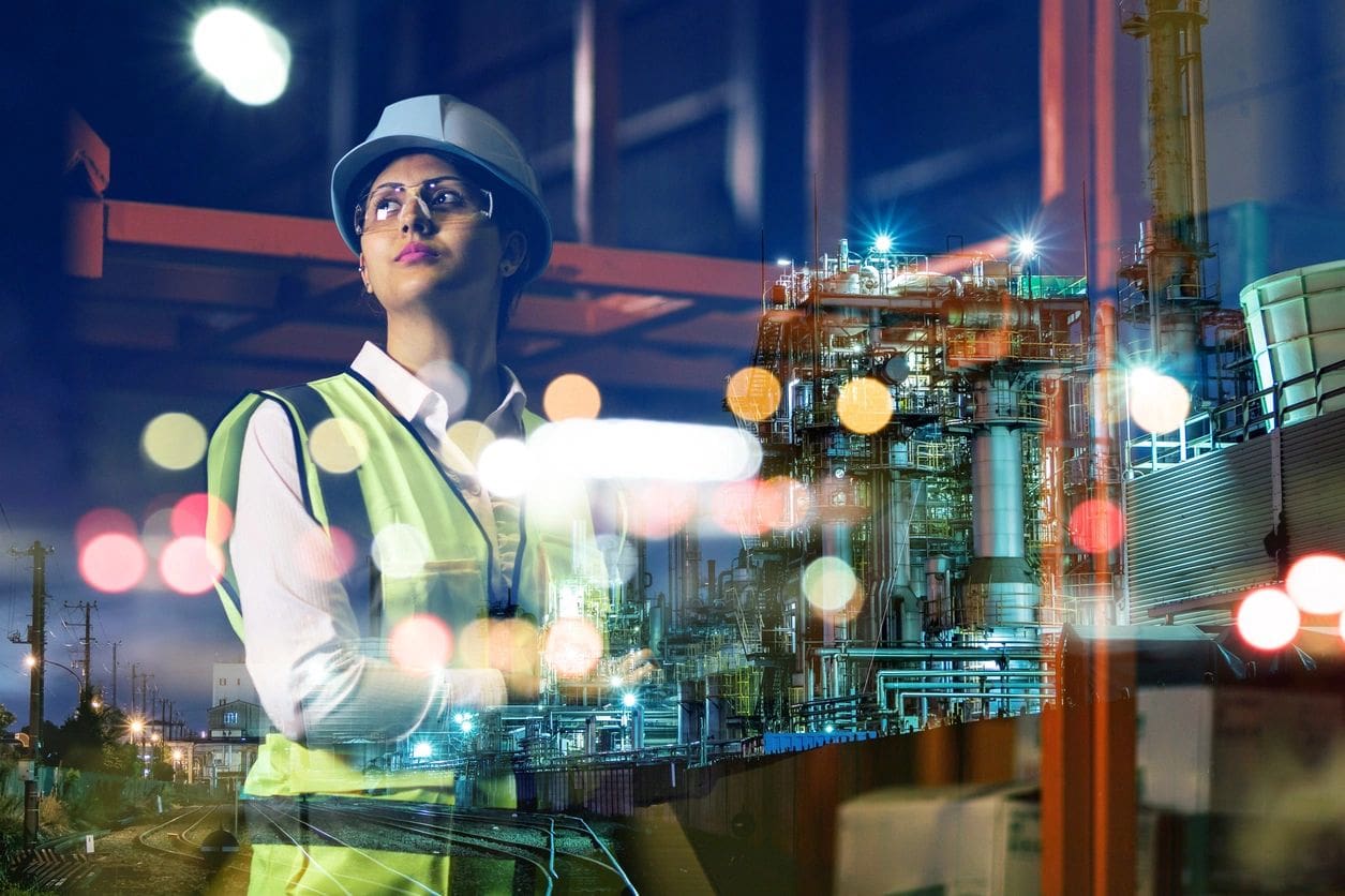 Person in a high-visibility vest and hard hat in a factory setting, with overlay of industrial plant machinery and lights in the background.